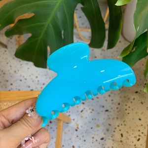 Macro detail of large glossy bright blue hair claw clip being held to show size and scale