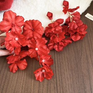 Close-up of red silk flower earrings with pearls and gold chains on a plush background