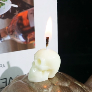 Lighted white skull-shaped scented candle on golden textured base for Halloween decor