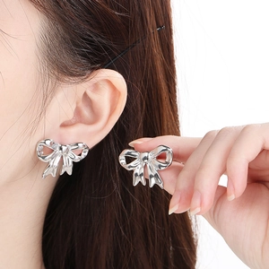 Detail of silver bow earrings in polished stainless steel shown as a pair on model