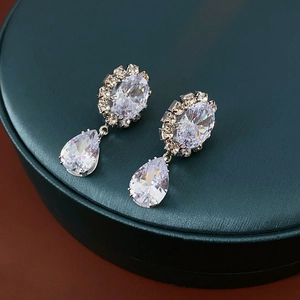 Detail of silver drop earrings featuring oval and teardrop zircon stones on a green surface