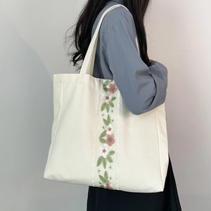 Vista laterale della borsa tote in tela bianca con ricami floreali indossata da modella