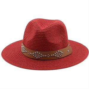 Detail of red straw fedora hat featuring a brown studded leather band and fine weaving
