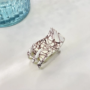 Détail d'une pince à cheveux blanche à lignes abstraites noires sur fond minimaliste