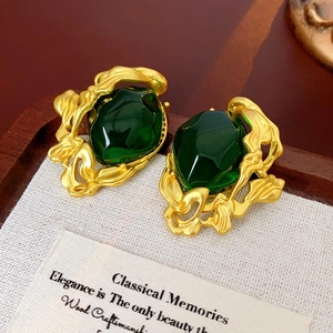 Detail of vintage gold earrings with emerald green gemstones on beige fabric and wood