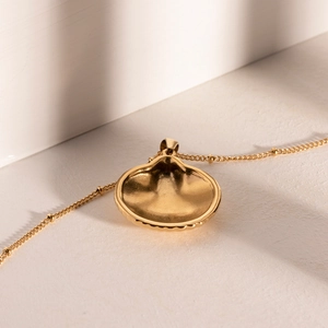 Detail of a gold scallop shell pendant with ball bead chain on a textured surface