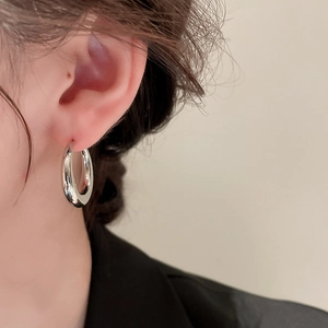 Close-up of minimalist silver-tone C-shaped hoop earrings on model showing mirror finish