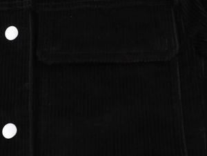 Détail de la texture en velours côtelé noir et bouton blanc rond sur la poche
