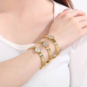 Trois bracelets trèfle dorés avec nacre et cristaux portés en superposition au poignet
