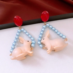 Detailed close-up of rabbit pendant earrings with red resin beads and faux pearls