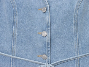 Détail des boutons argentés gravés et des surpiqûres orange sur denim bleu clair
