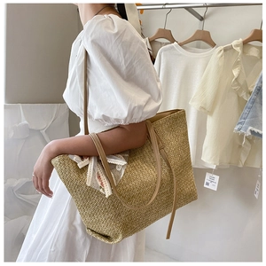 Detail of a large straw tote bag with brown leather handles and white floral lace ribbon