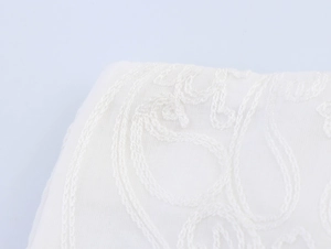 Close-up detail of white lace embroidery on cotton linen fabric shorts with floral texture