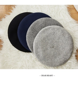 Flat lay of four classic wool beret hats in black and grey tones on soft faux fur