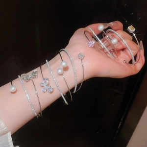 Close-up of sparkling cubic zirconia and pearl floral open bracelets on model's wrist