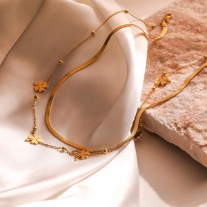 Double-layered gold clover necklace with snake chain on white silk and marble stone