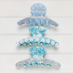 Three sea-shell acetate hair claws in blue marble and rhinestone designs on white wood