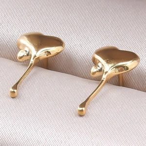 Close-up of golden stainless steel heart and teardrop drop earrings on beige fabric