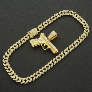 Détail de luxe du pendentif pistolet doré serti de zircons sur une chaîne cubaine