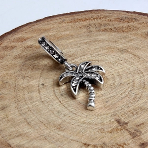 Silver palm tree charm pendant with sparkling crystals on a natural wood slice background