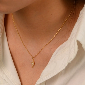 Detailed view of a gold lighting bolt pendant necklace with zircons on a female model