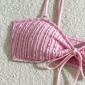 Detailaufnahme des rosa strukturierten Bikini-Oberteils mit Kordelzug auf weißem Vlies