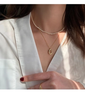 Detail of layered 925 silver gold chain with pearls and oval donut pendant on model