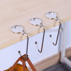 Three silver metal desk bag hooks attached to a wooden table with a brown backpack