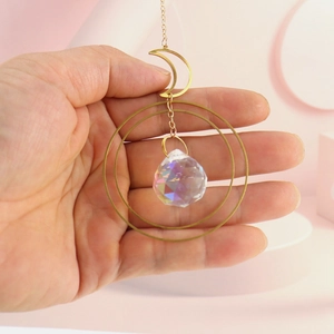 Detail of hand holding a golden moon suncatcher with multifaceted iridescent crystal ball