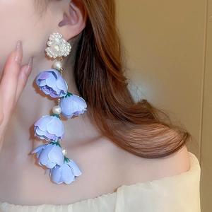 Dettaglio di orecchini lunghi con nappe, fiori viola e perni a cuore di perle