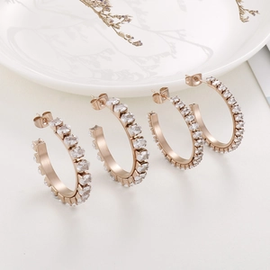 Close-up of rose gold C-shaped earrings with oval white zircon inlays on white ceramic