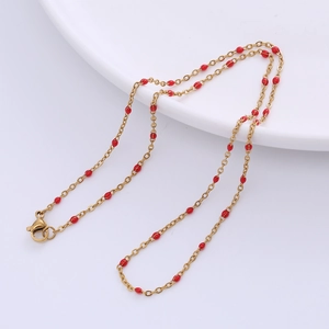Detail of a golden chain necklace with small red beads and a secure lobster clasp
