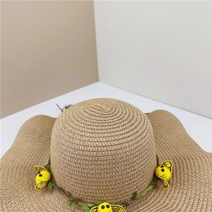 Détail d'un chapeau de paille à large bord orné de lianes vertes et de petites abeilles