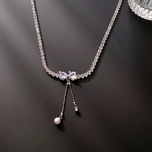 Detailed view of silver bow necklace with zircon stones and pearl fringe droplets