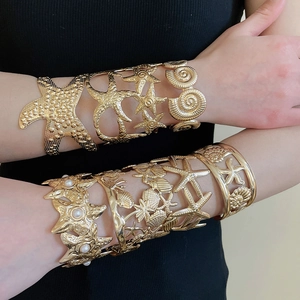 Close-up of gold metal starfish and seashell open bracelets with white pearls on a model