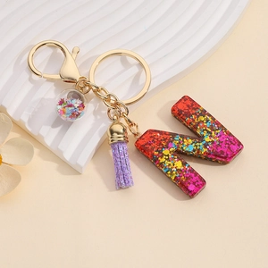 Detail of resin letter N keychain with red sequins, star ball, and purple tassel charm