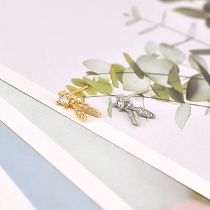 Detail shot of gold and silver leaf-shaped earrings with zircon accents on nature background