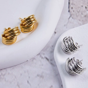 Orecchini geometrici minimalisti in oro e argento su un vassoio di pietra bianca