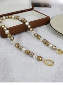 Detail of mixed-color pearl necklace with golden metal clasps on a white fabric background