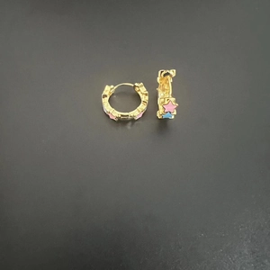Close-up of golden hoop earrings featuring pink and blue star patterns on dark background