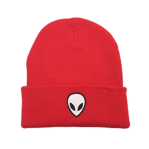 Detail of red knitted beanie featuring white alien skull embroidery on ribbed cuff