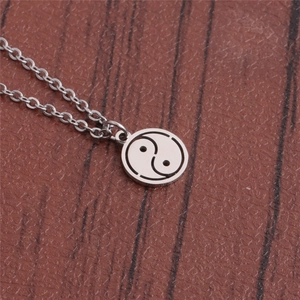 Detailed view of a polished stainless steel Bagua Yin Yang pendant on a wood surface