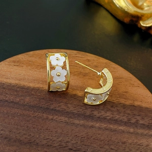 Detail view of gold-plated C-shaped earrings with delicate white flowers on wooden stand