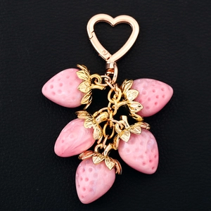 Detail of five pink resin strawberries on a golden heart-shaped clasp keychain