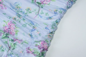 Detail view of light blue floral dress fabric with purple blooms and elastic smocking