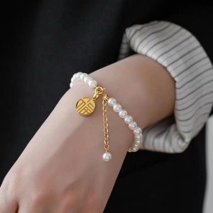 Detail of 18K gold-plated lucky charm pendant and pearl bracelet on a model's wrist