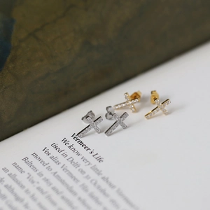 Close-up of gold and silver cross stud earrings with micro-pave crystals on a book