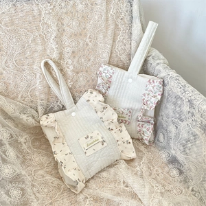 Detail of quilted cotton wrist bag with floral ruffles and a snap button on lace background