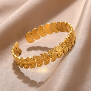 Detail of gold-plated open cuff bracelet with laurel leaf pattern on silk background