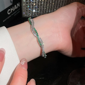 Nahaufnahme eines verdrehten 18k vergoldeten Armbands mit grünen Zirkonia-Steinen